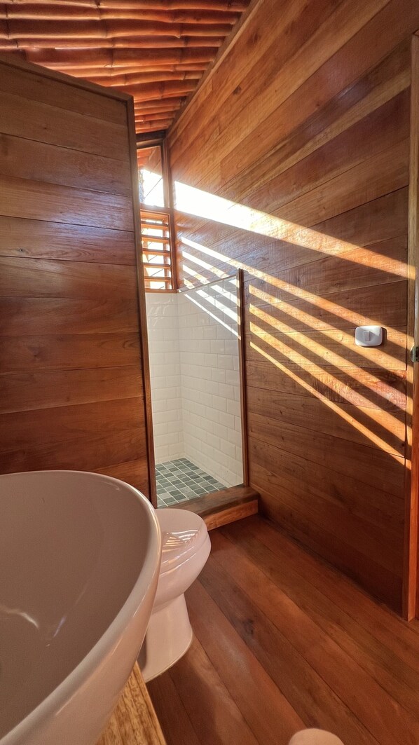 A wooden interior with a toilet, a large white basin, and a small window.