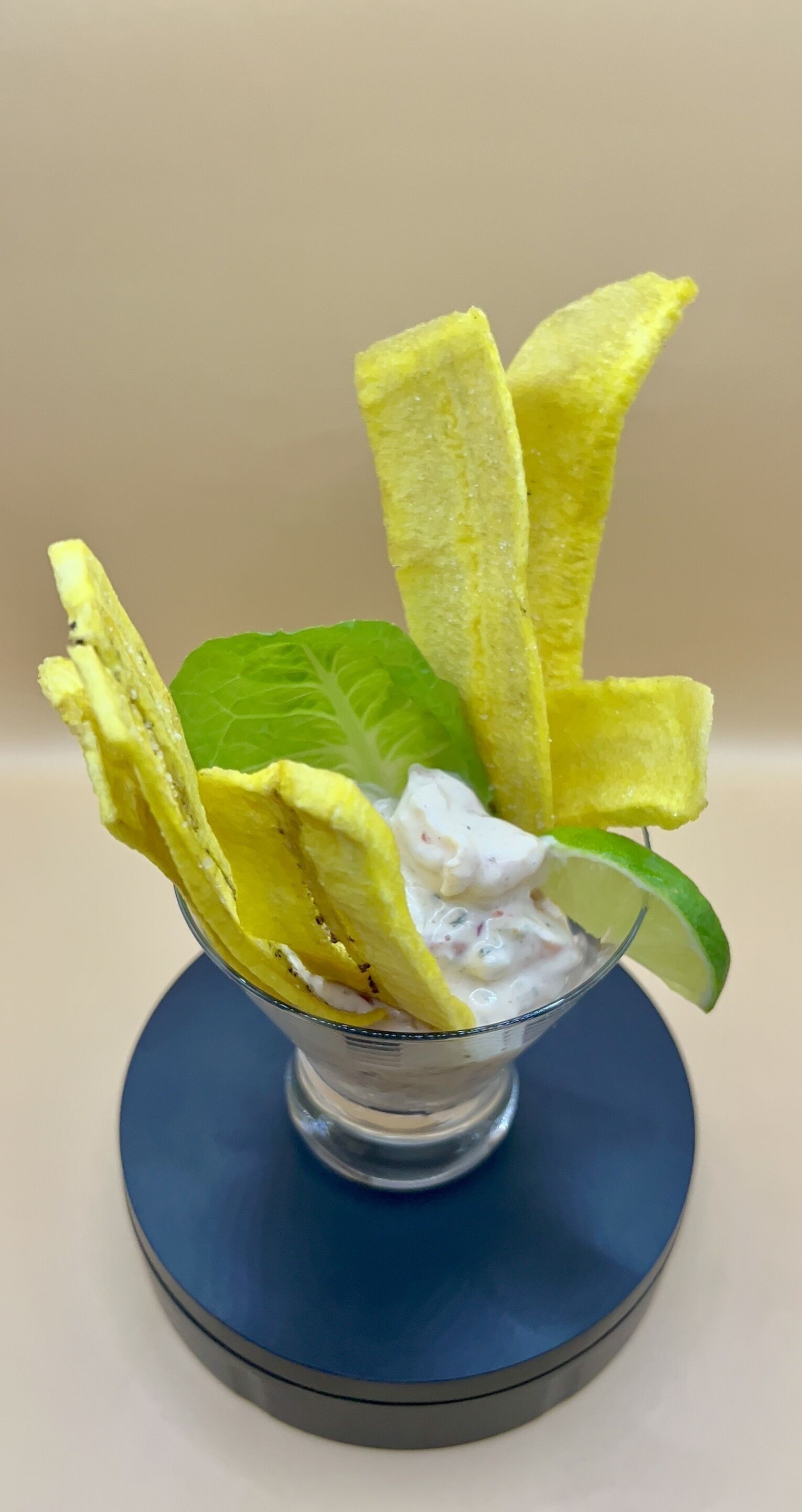 A dessert in a glass bowl with yellow wafer sticks and a lime slice on a blue plate.