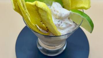 A dessert in a glass bowl with yellow wafer sticks and a lime slice on a blue plate.