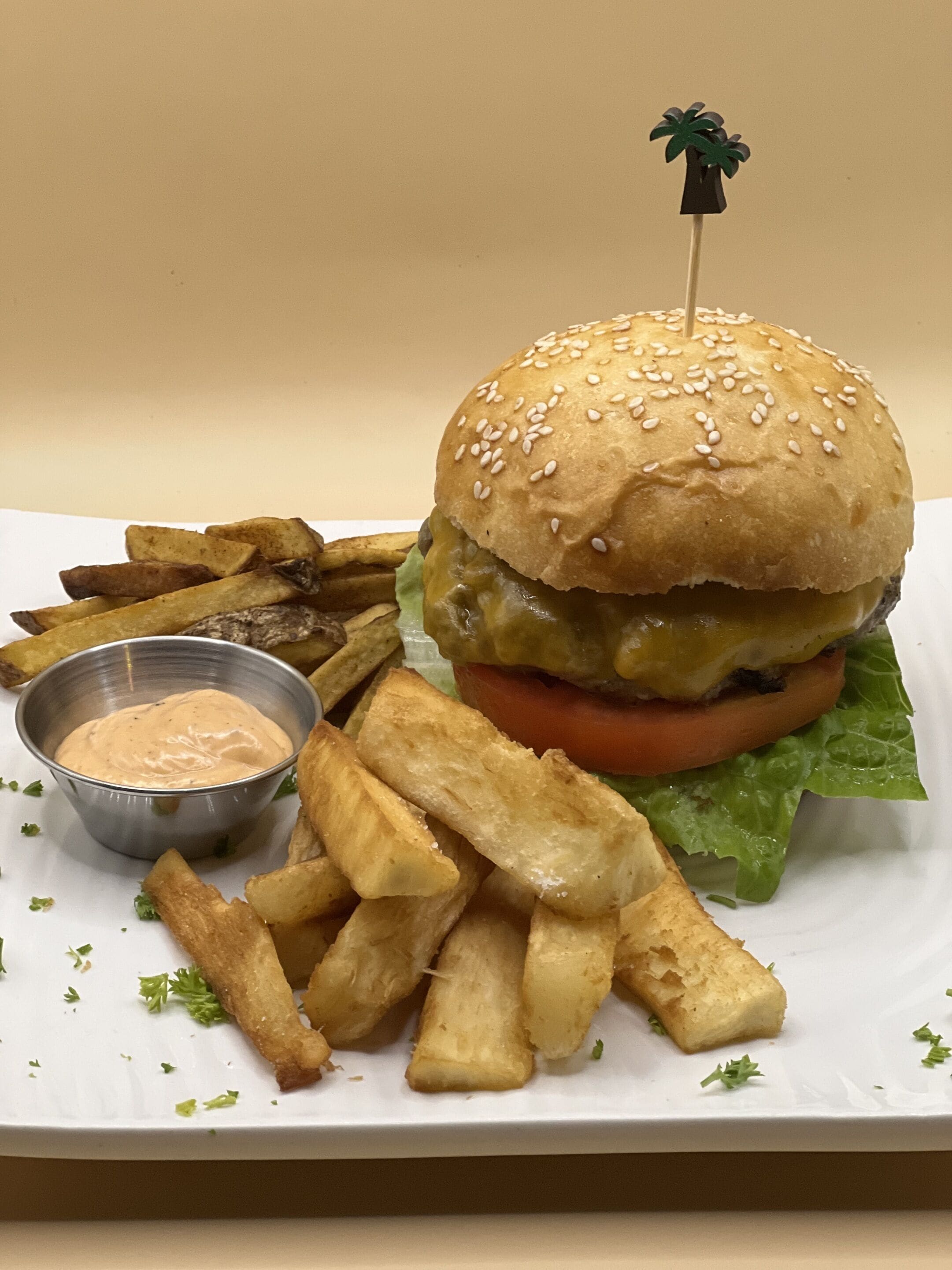 Hamburguesa con pan de sésamo, lechuga, tomate y queso, acompañada de papas fritas y salsa para mojar.