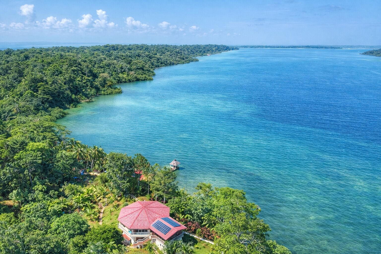 Um imóvel costeiro com um edifício de telhado vermelho, rodeado por vegetação exuberante e águas azul-claras.
