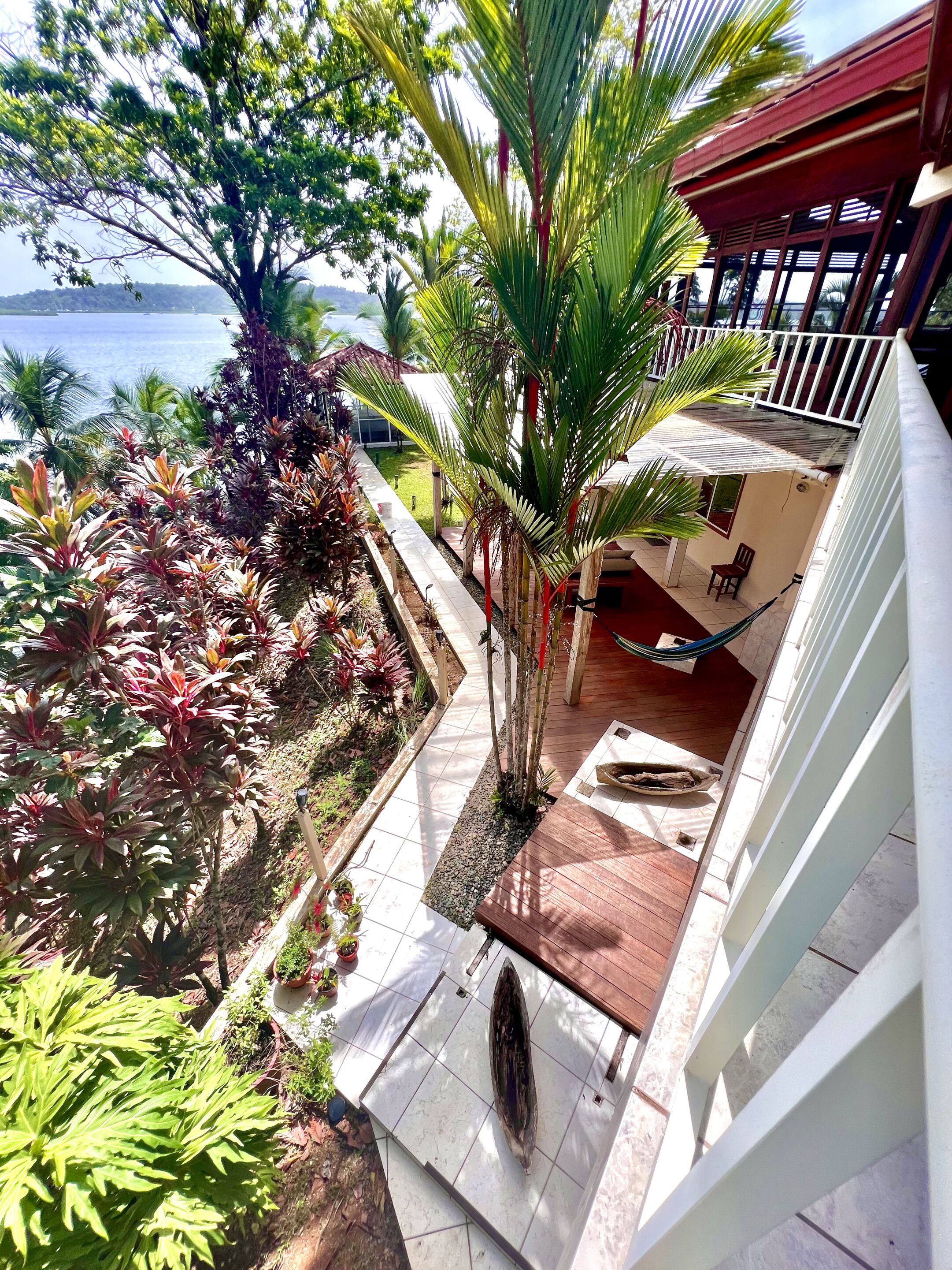 A balcony with a view of the sea, surrounded by tropical plants and a hammock.