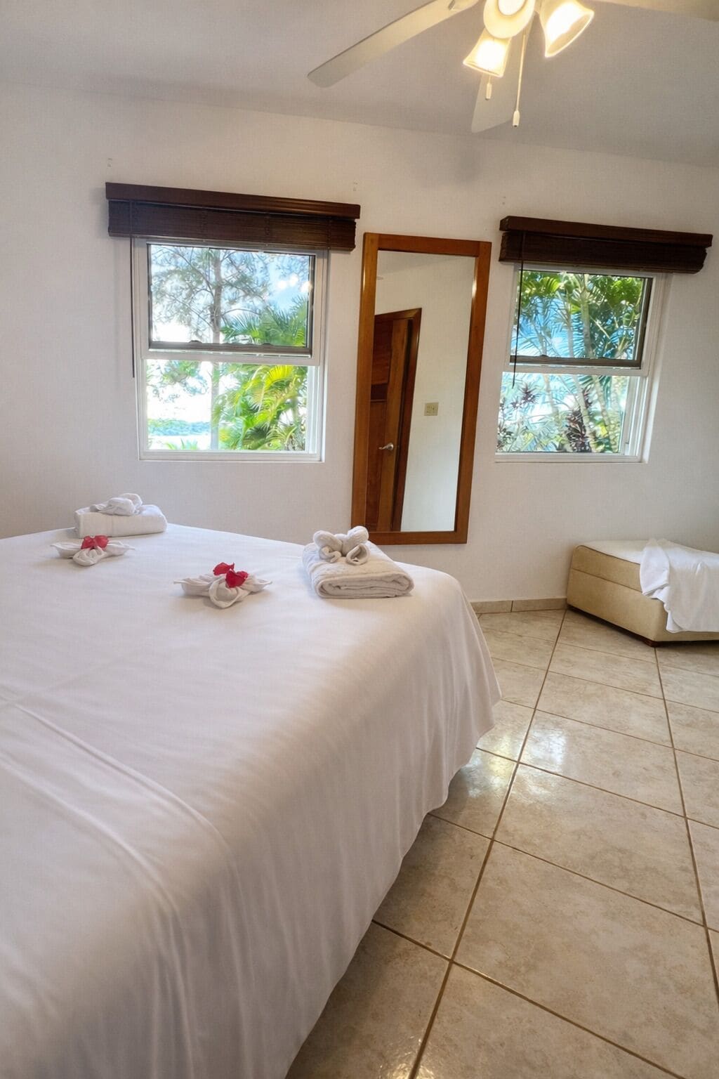 Una habitación de hotel con una cama grande, dos ventanas, un ventilador de techo y una puerta.