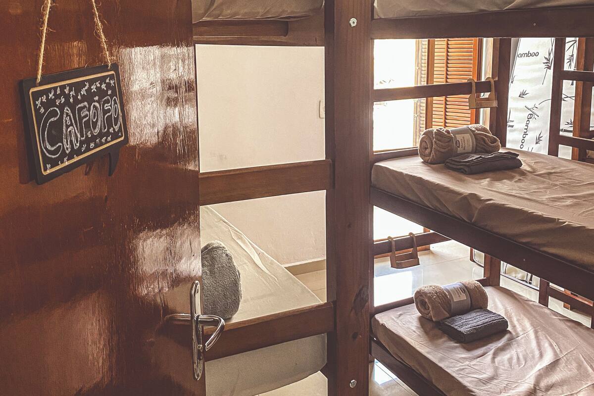 Habitación con literas de madera, un letrero en la pared y una ventana con contraventanas de madera.