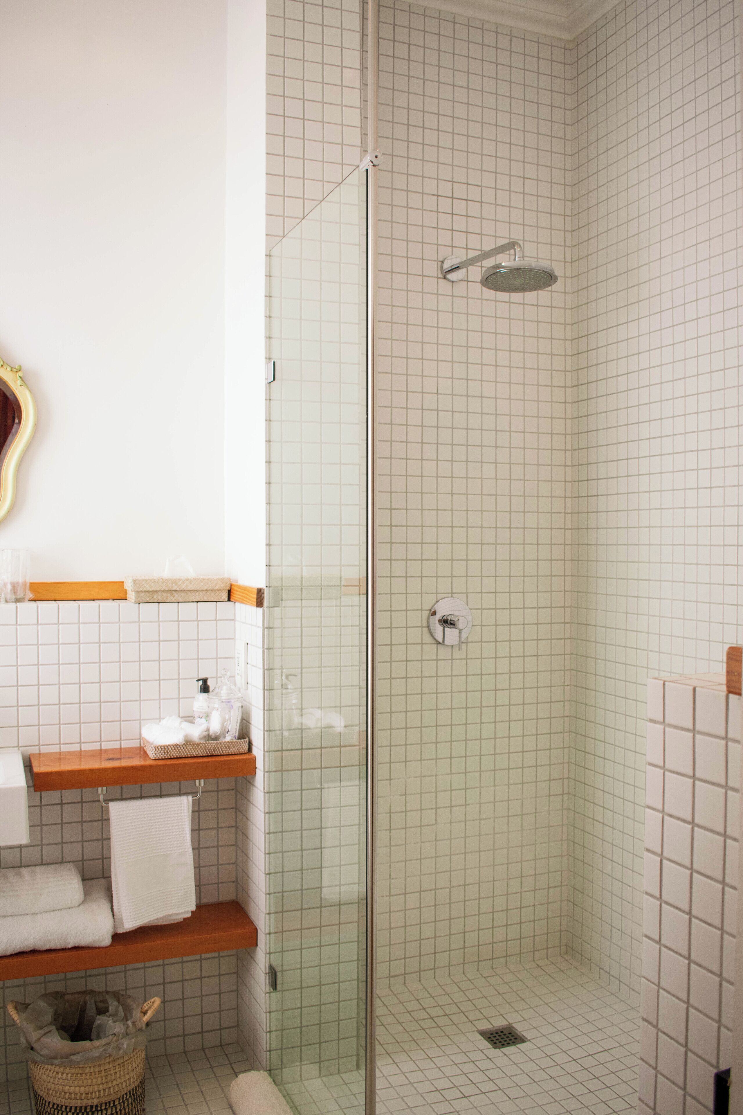 Una ducha con puerta de vidrio, un estante de madera con toallas y una pequeña cesta en el suelo.