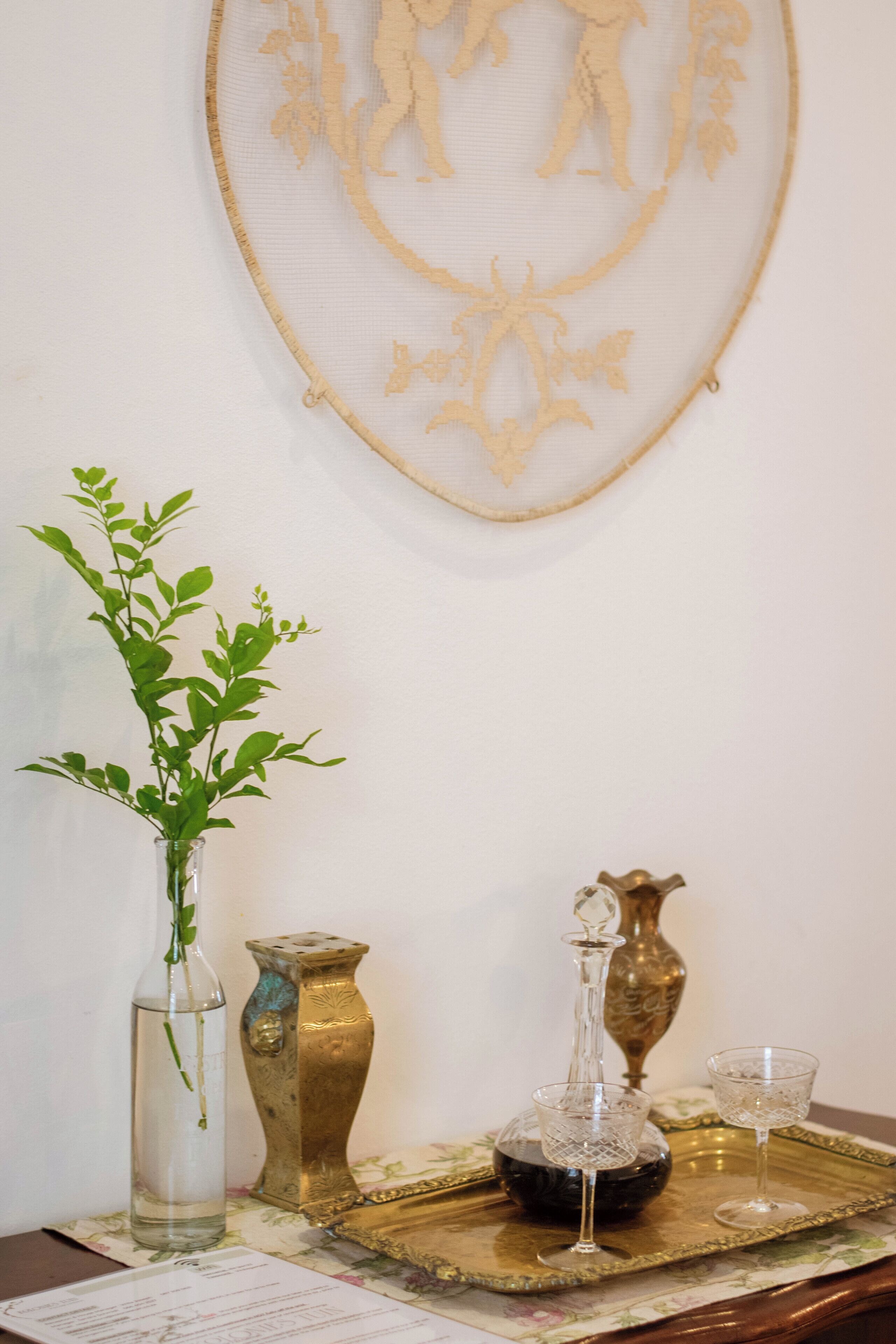 A table with a vase of green leaves, a decorative plate, and two glassware items.