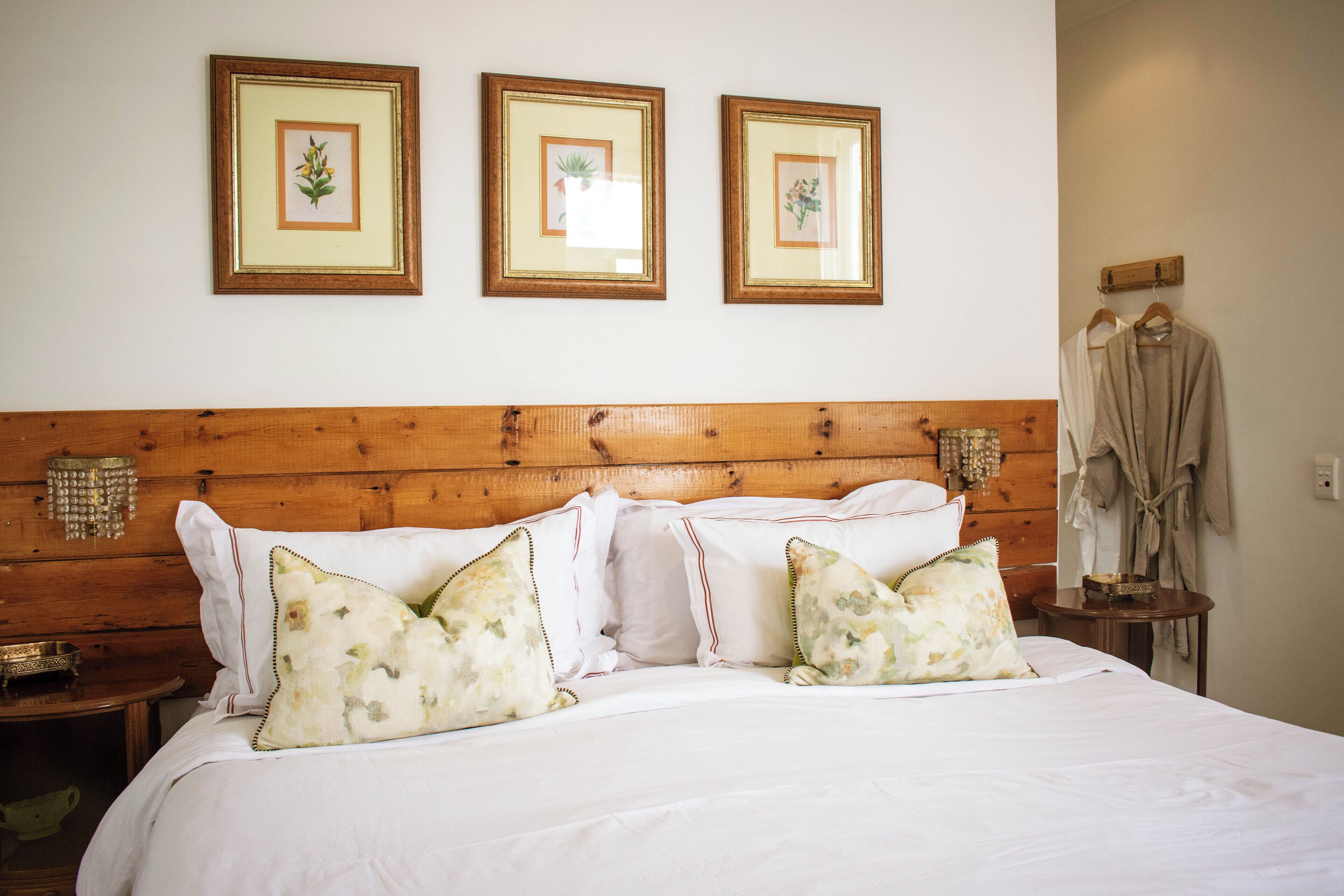 Una cama bien hecha con almohadas estampadas con motivos florales, un cabecero de madera y tres cuadros en la pared.