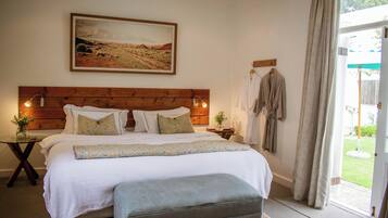 A bedroom with a large bed, a wooden headboard, a painting above the bed, a nightstand with a lamp, and a view of the outdoors through a door.