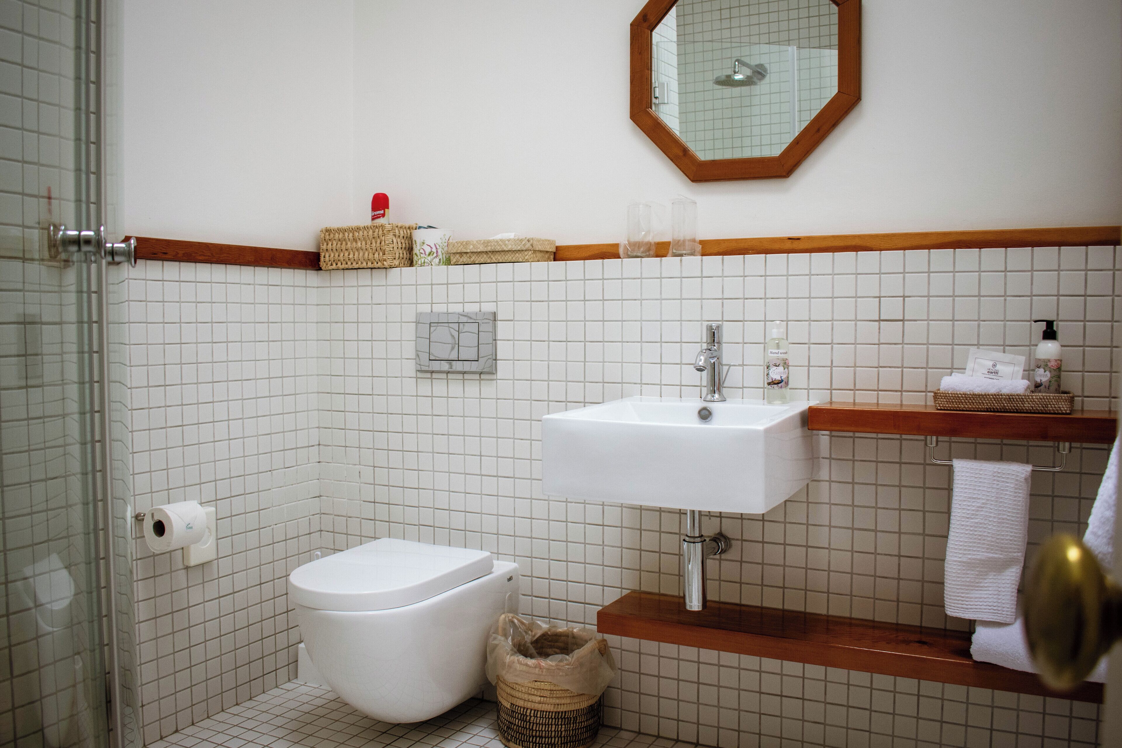 A bathroom with a white tiled wall, a white sink, a wooden vanity, a mirror, and a toilet.