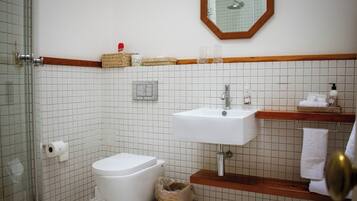 A bathroom with a white tiled wall, a white sink, a wooden vanity, a mirror, and a toilet.