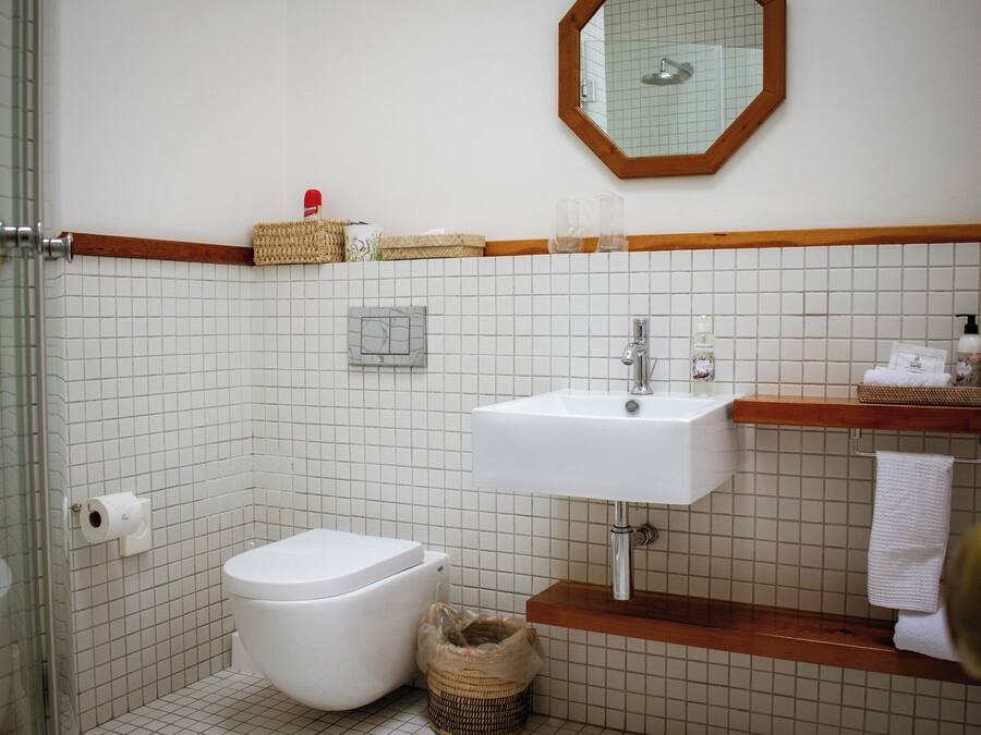 A bathroom with a white tiled wall, a white sink, a wooden vanity, a mirror, and a toilet.