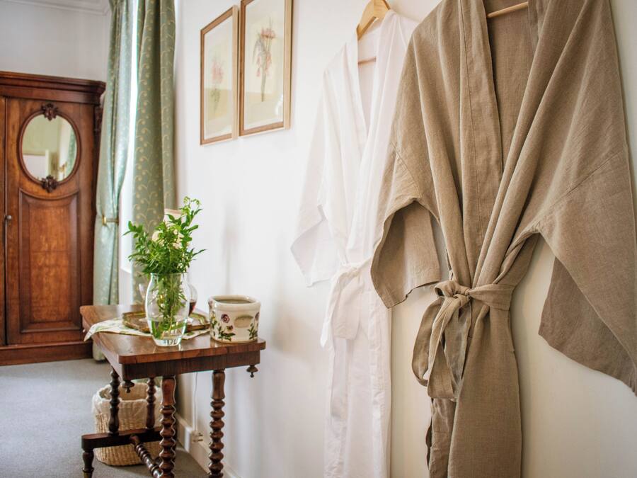 A room with a wooden wardrobe, a table with a vase and a cup, and a robe hanging on the wall.
