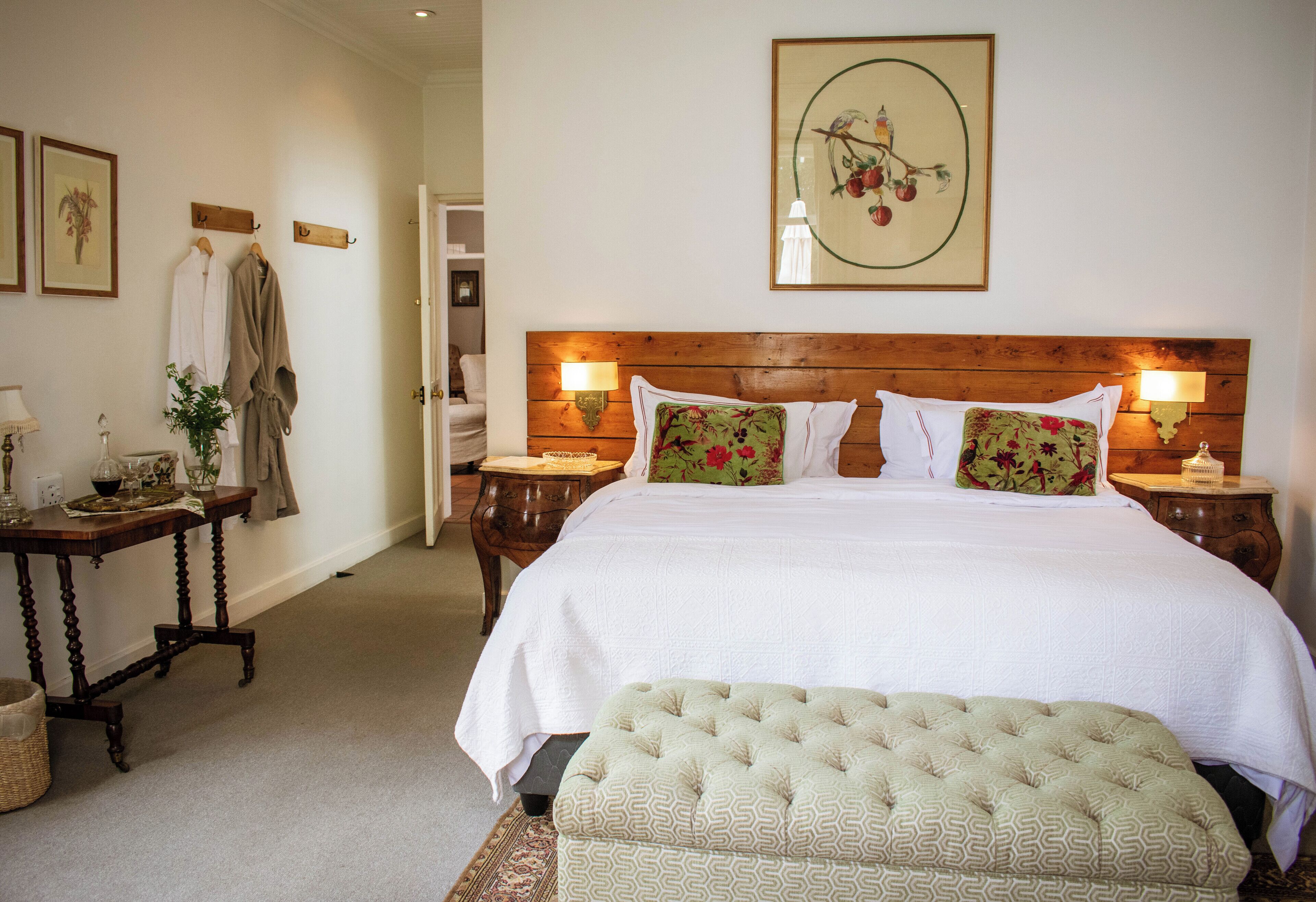 A neatly arranged bedroom with a large bed, two bedside tables, a wooden headboard, and a hanging robe rack.