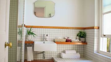 Un baño con lavamanos blanco, repisas de madera, un espejo y una bañera.