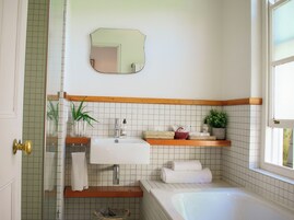 Un baño con lavamanos blanco, repisas de madera, un espejo y una bañera.