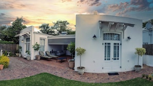 A white house with a covered patio, a fenced yard, and a brick pathway. - Kolonies Tuin (Stellenbosch)