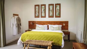 Une chambre à coucher avec une tête de lit en bois, une couvre-lit matelassée verte, un banc en osier et trois œuvres d’art encadrées accrochées au mur.