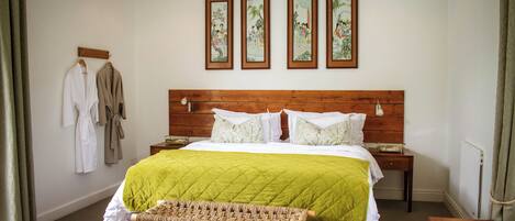 Une chambre à coucher avec une tête de lit en bois, une couvre-lit matelassée verte, un banc en osier et trois œuvres d’art encadrées accrochées au mur.