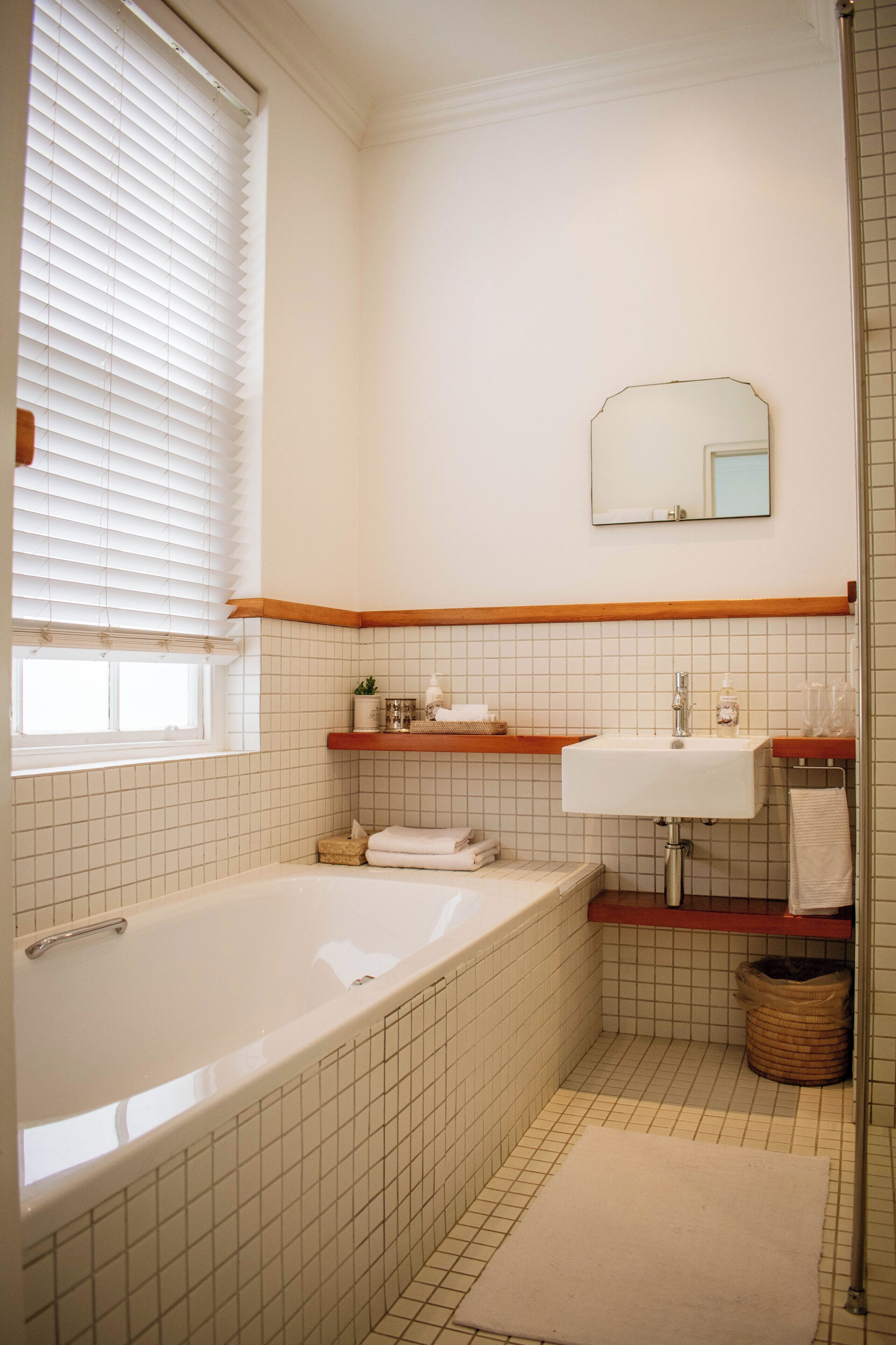 Un bagno con una vasca, un lavandino, uno specchio e una finestra con persiane.