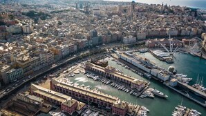 An aerial view of a coastal city with a marina, historic buildings, and a Ferris wheel.