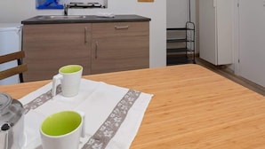A compact kitchen with a wooden countertop, a sink, and a small cabinet. There is a table with two mugs and a kettle.