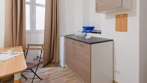 A compact kitchen with a sink, a small refrigerator, and a wooden table with a chair.