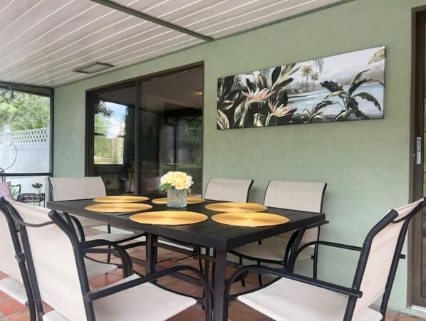 A dining area with a black table and beige chairs, a vase with flowers, and a painting on the wall. - Poolside Family Retreat- Near the Springs & Ocala National Forest. Pet friendly (Ocklawaha)