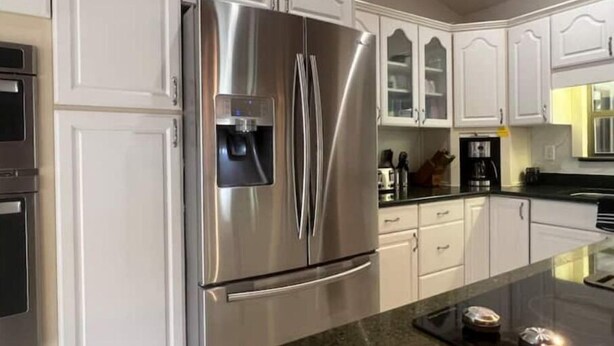 Una cocina moderna con armarios blancos, un refrigerador de acero inoxidable y una encimera de granito.