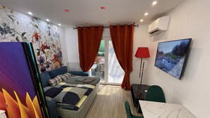 Ein modernes Hotelzimmer mit Schlafsofa, Esstisch, roter Lampe und einem Bild an der Wand.