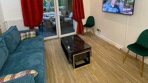 Ein modernes Wohnzimmer mit einem Türkis-farbenen Sofa, einem schwarzen Couchtisch, roten Vorhängen und einem Fernseher an der Wand.