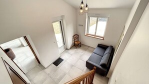 Un vaste espace de vie comprenant un canapé gris, un fauteuil en bois et un escalier menant à l’étage supérieur.