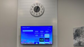 Un salon moderne avec une horloge murale, un téléviseur à écran plat affichant l’interface d’un service de diffusion en continu et une cheminée située sous le téléviseur.