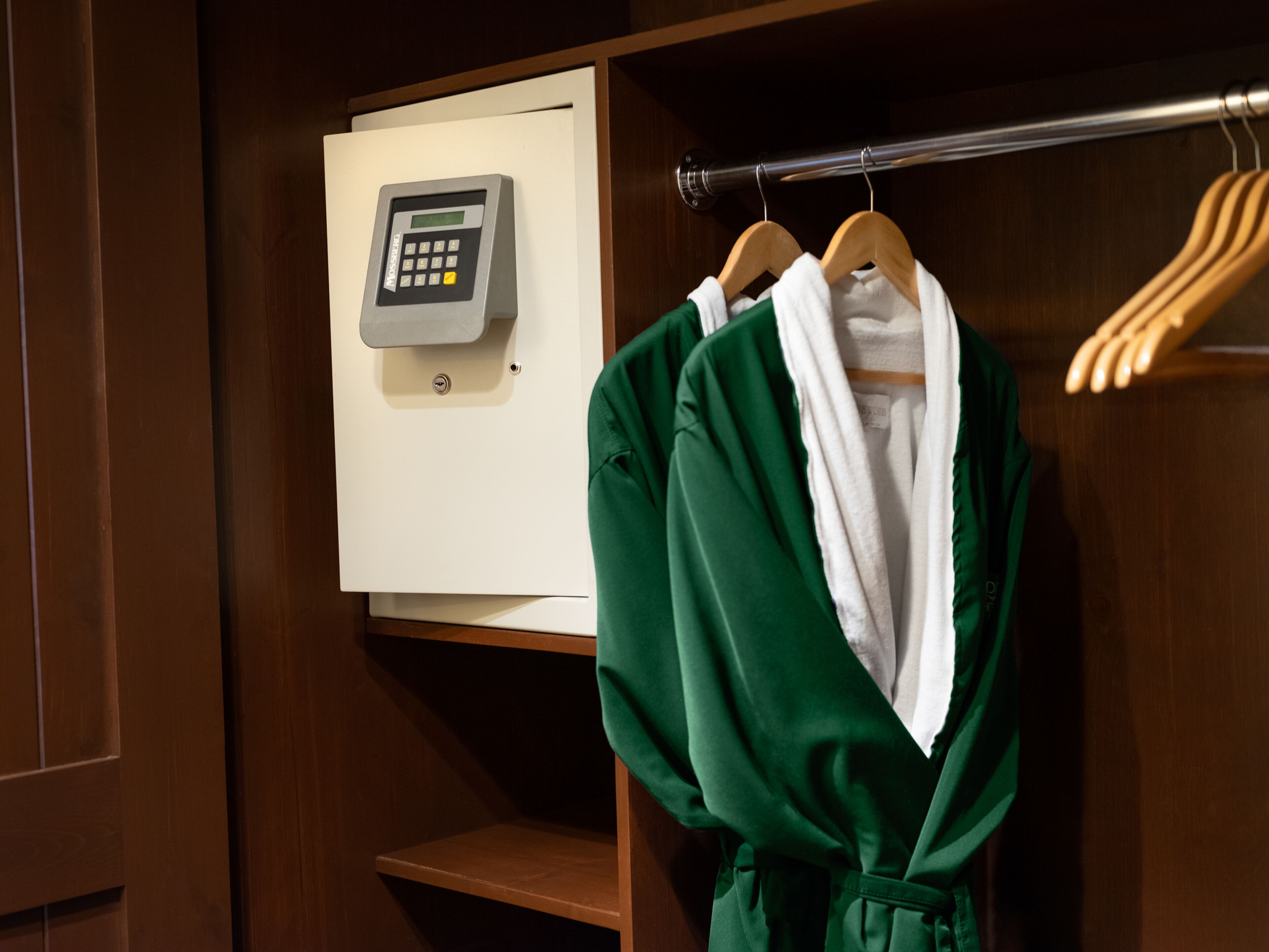 A wooden wardrobe with a built-in safe and a robe hanging on a wooden hanger.