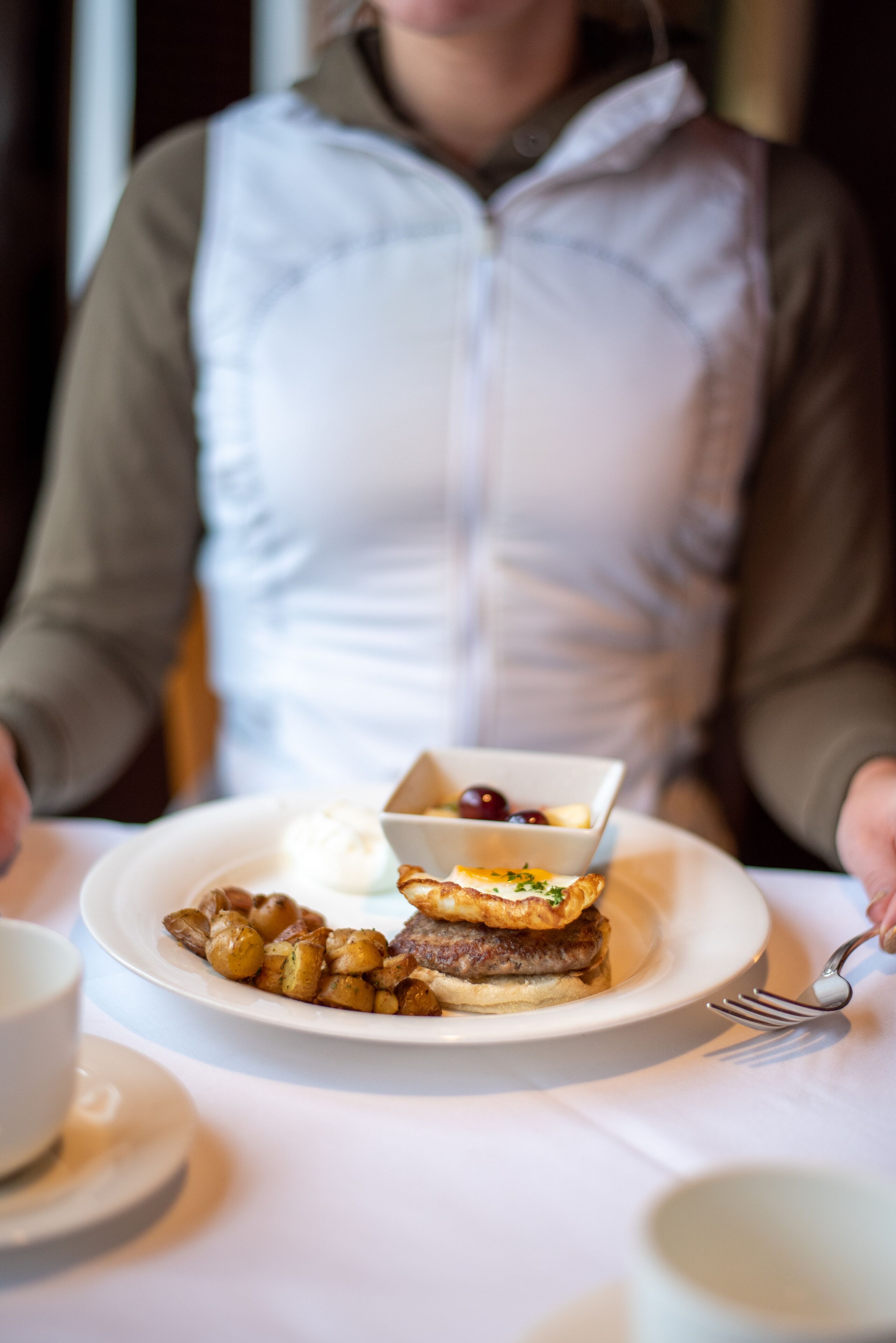 Une personne est assise à une table devant une assiette de nourriture, comprenant un sandwich et des pommes de terre.