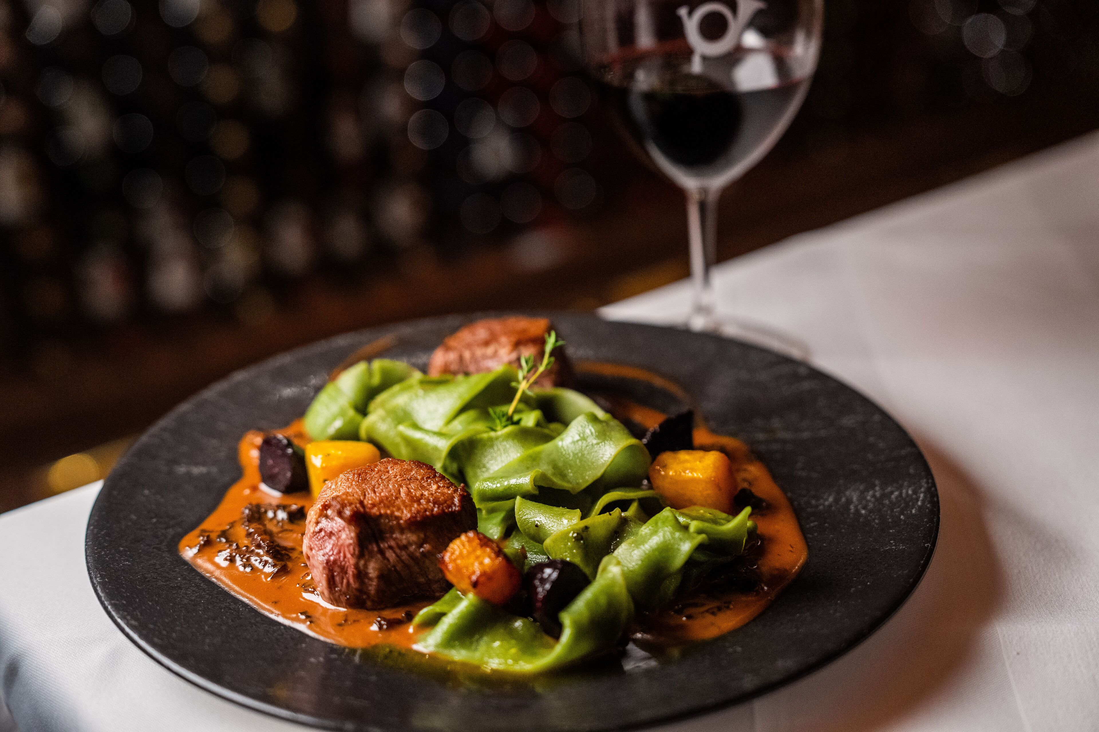 Une assiette de nourriture avec un verre de vin rouge en arrière-plan.