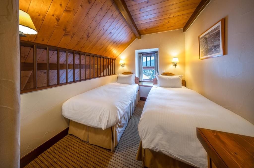 Une chambre avec deux lits simples, des murs en bois, un plafond en pente et une fenêtre donnant sur un beau paysage.