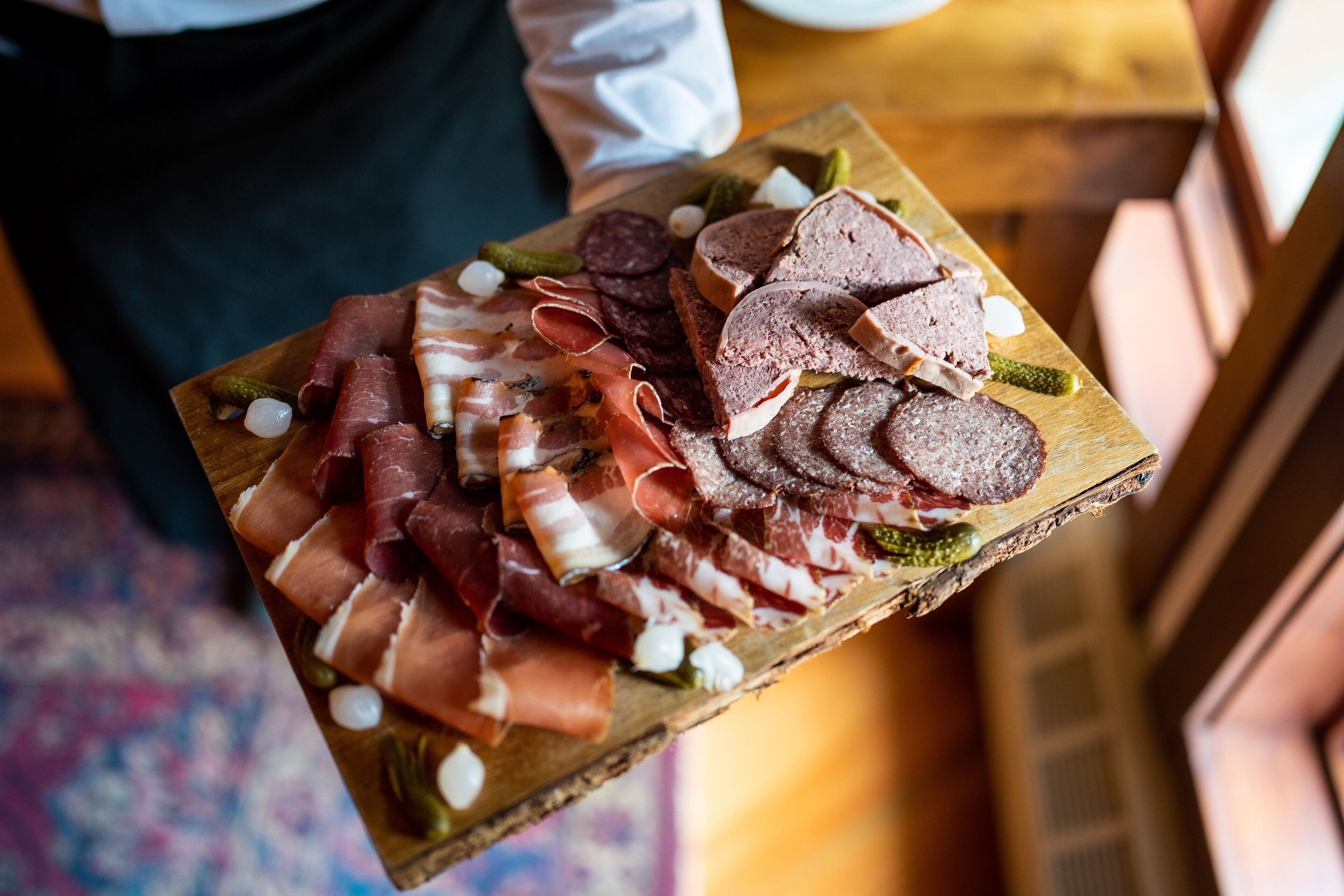A wooden board with various types of cured meats and pickles.