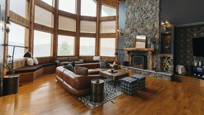 A spacious living room with a large stone fireplace, wooden beams, and a cozy seating area. - Among the Trees - The Lodge (Logan)