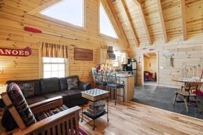 Interior acogedor de una cabaña con detalles de madera, un sofá, una mesa de comedor y una zona de cocina.