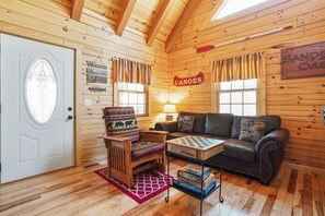 Un interior de cabaña acogedor con paredes de madera, una chimenea, un sofá, una silla de madera y una mesa para jugar al ajedrez.