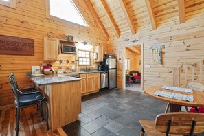 A wooden cabin interior with a kitchen, dining area, and a sign reading "INDSTONE OASIS". - Sandstone Oasis | Hocking Hills, Couples, Hot Tub (Logan)