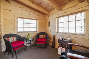 L’intérieur d’un chalet accueillant, avec deux fauteuils en osier dotés de coussins rouges, une petite table et un banc en bois.
