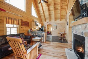 A cozy cabin interior with a fireplace, wooden furniture, a dining area, and a kitchen. - Sandstone Oasis | Hocking Hills, Couples, Hot Tub (Logan)