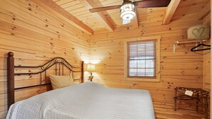 En stuga med träpanel, ett rum med en säng, ett fönster med persienner, en hängande lampa och ett litet bord med en skylt.
