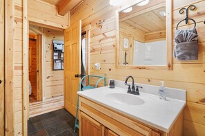 A wooden cabin bathroom with a sink, mirror, towel rack, and a door leading to another room. - Sandstone Oasis | Hocking Hills, Couples, Hot Tub (Logan)