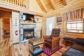 L’intérieur chaleureux d’un chalet avec une cheminée en pierre, des murs en bois, une table à carreaux et un fauteuil à motifs.