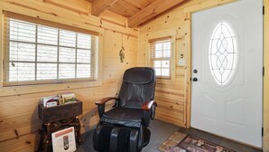 En stuga med träpanel på insidan, komplett med en massagestol, ett litet bord med böcker och en dörr med en dekorativ glaspanel.