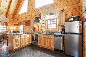 A wooden cabin interior with a kitchen featuring a stainless steel refrigerator, a dishwasher, a microwave, and a stove.