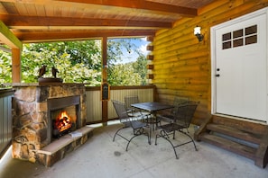 A stone fireplace with a fire, a wooden deck, a table with chairs, and a white door.