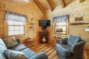 A cozy cabin interior with wooden walls, a fireplace, a television, and two sofas.